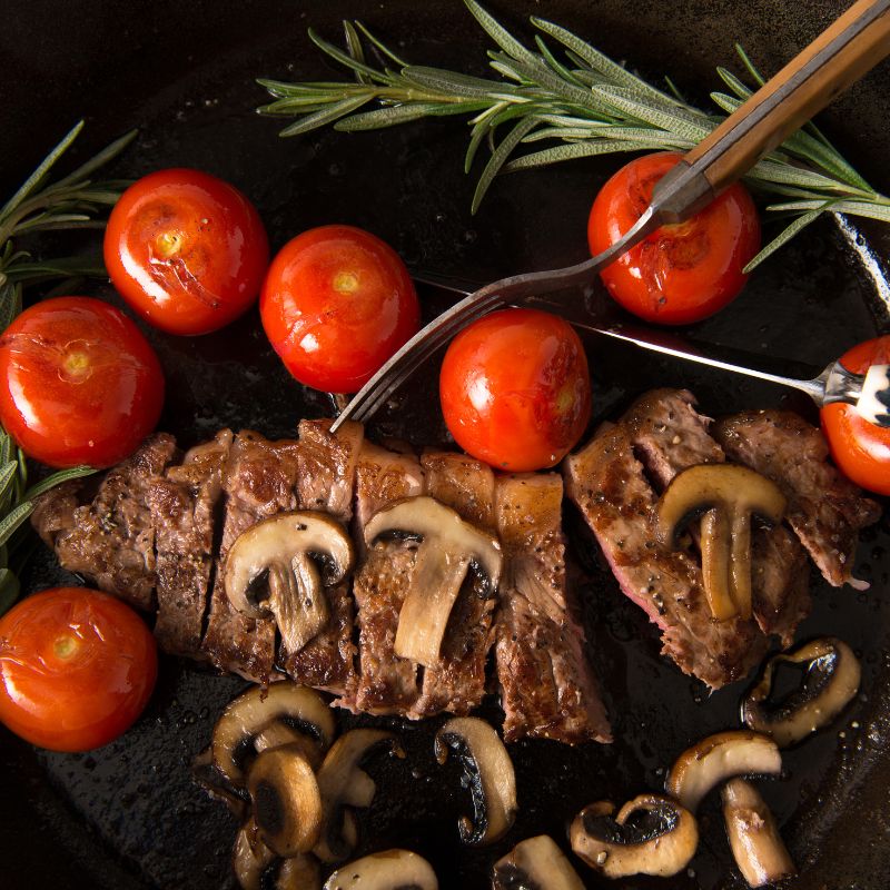 Sliced Australian AMG Grass Fed  Steer Striploin with mushrooms and tomatoes on a black surface