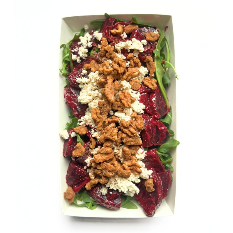 A top-down view of Beetroot Salad with Tofu Cream Cheese & Sprouted Maple Walnuts in a white rectangular paper container, featuring dark red beets, green spinach leaves, crumbled white cheese, and walnuts on a white background.