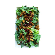 A top-down view of Crispy Romaine Salad with Pomegranate, House Cashew Sour Cream & Garlic-Herb Sprouted Walnuts in a white rectangular container, featuring crisp lettuce leaves, crunchy walnuts, and red pomegranate seeds on a white background.