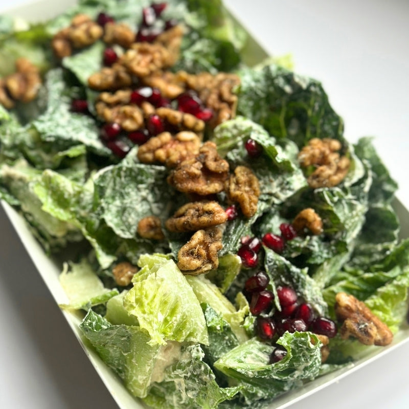 A close-up of a Crispy Romaine Salad with Pomegranate, House Cashew Sour Cream & Garlic-Herb Sprouted Walnuts in a white rectangular container, topped with chopped walnuts and pomegranate seeds.

(380g | Serves 4-6)
Foodcraft Online Store 