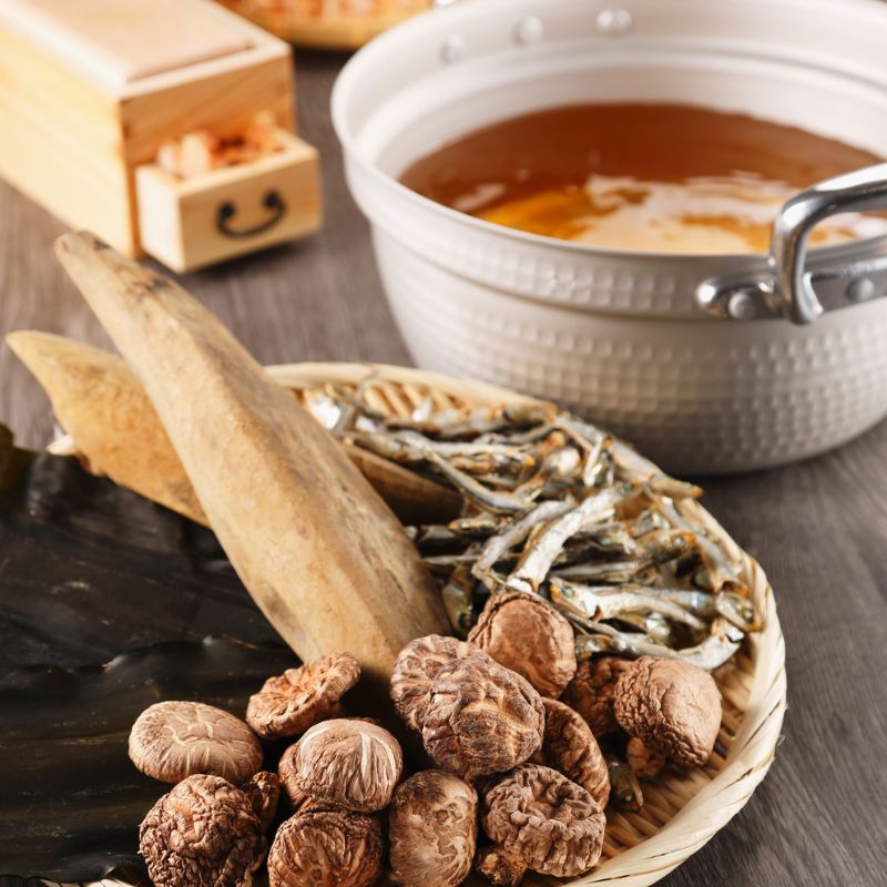 Dashi Broth Pack ingredients in a woven basket with a pot of dashi soup in the background.