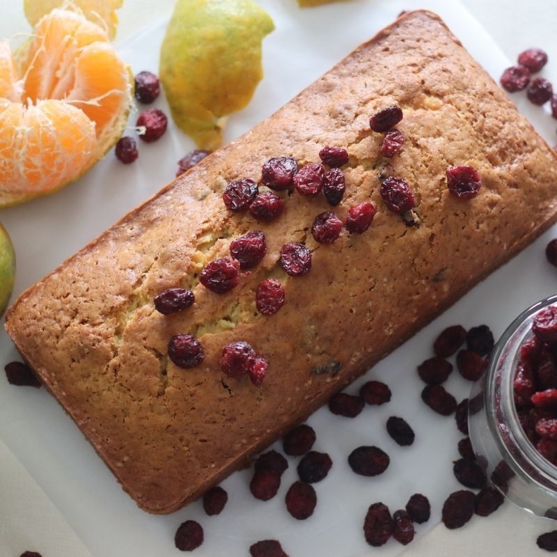 Loaf of bread with dried cranberries on a white surface with fruits around