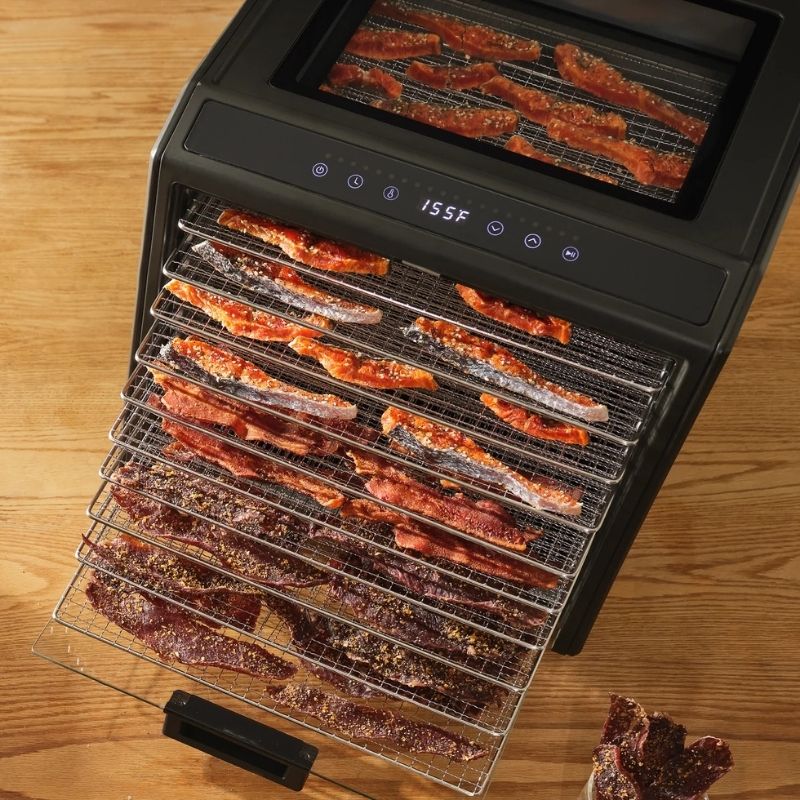Excalibur 10 Tray Performance Digital Dehydrator, in Stainless Steel - DH10SSSS13 with multiple wire trays loaded with sliced meats, shown on a wooden tabletop with the door pulled open.