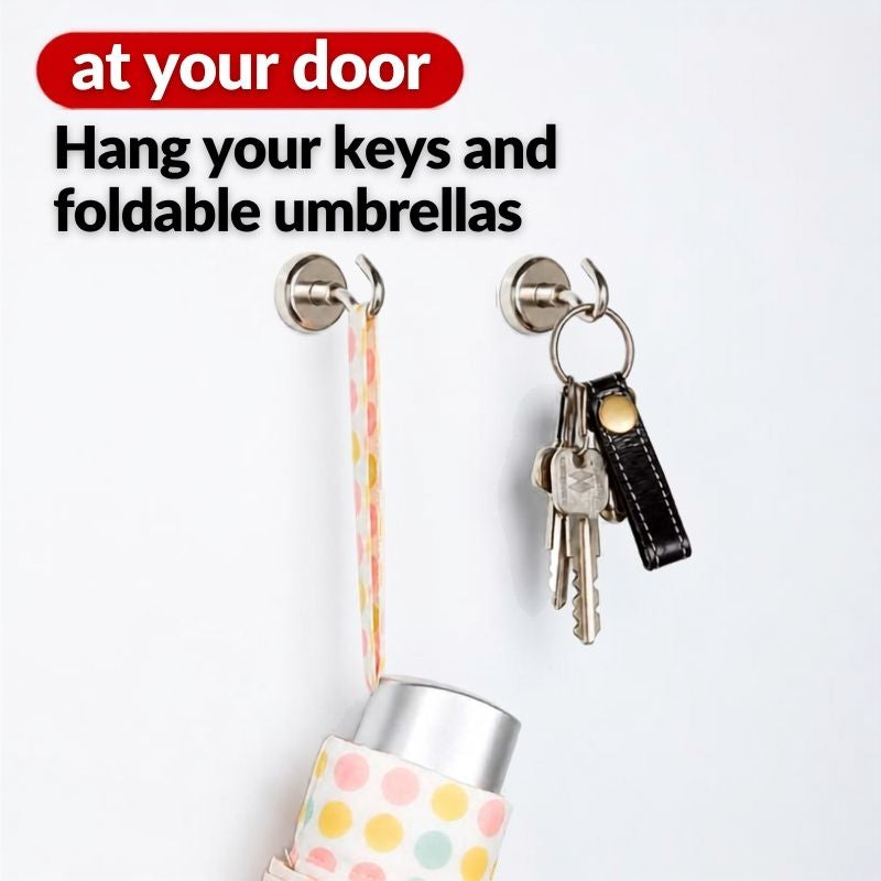 A set of two Shimomura Kihan Heavy Duty Neodymium Magnetic Hooks - Set of 5 (model number 44638) on a white wall, shown with text reading 'at your door' and 'Hand your keys and foldable umbrellas.' One hook holds a set of keys with a black leather key fob, and the other holds a pastel polka-dot umbrella strap with part of a matching folded umbrella visible.