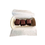 Three chocolate-covered Gluten Free Keto Dark Chocolate Coated Lemon Poppy Seed Cake - 150g pieces arranged in a paper box lined with white parchment paper, photographed on a plain white background.