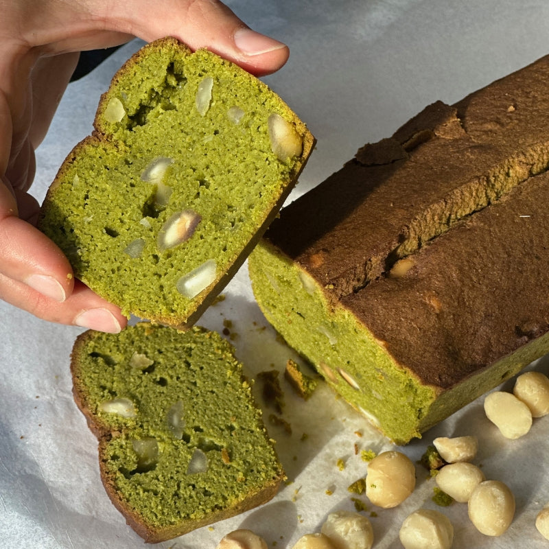 Gluten Free Keto Matcha Macadamia Cake with a slice being held, surrounded by macadamia nuts on a light background - Foodcraft online store