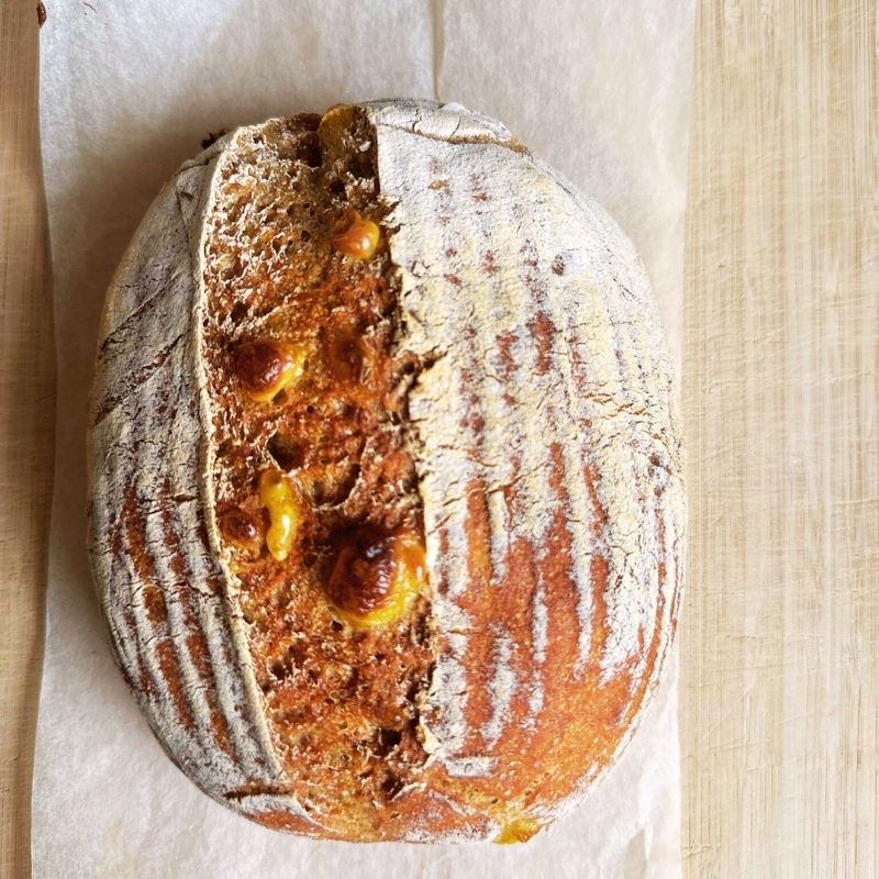 Loaf of luten Free Soft Sourdough Bread with Vegan Cheese with a cut section revealing the interior on a wooden surface