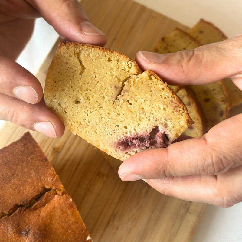 Close-up of hands holding a slice of Gluten Free Keto Raspberry Cake - 380g on a wooden cutting board.