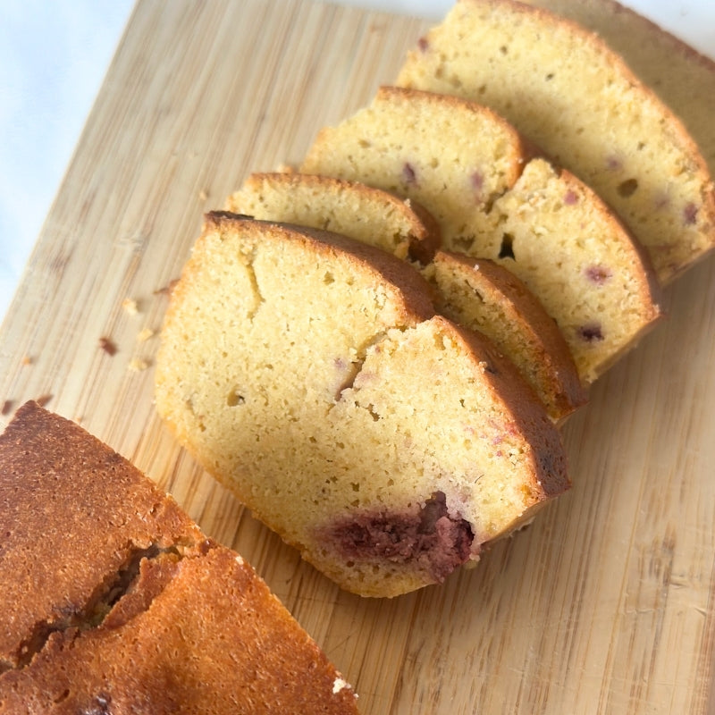 Sliced loaf of Gluten Free Keto Raspberry Cake - 380g, arranged on a light wooden cutting board.