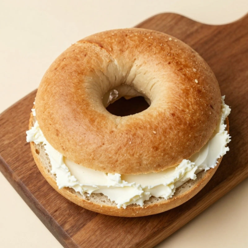 A sliced Gluten-Free Soft Original Sourdough Bagel  sandwich filled with thick white cream cheese, presented on a wooden cutting board against a light beige background.
Gluten-Free Soft Original Sourdough Bagel - Set of 2 - FoodCraft Online Store 