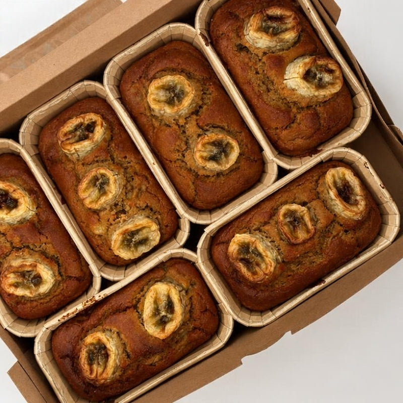 Six Gluten Free Vegan Banana Bread with Sprouted Walnuts - 120g Foodraft Online Store  loaves in individual brown paper trays arranged inside an open cardboard box, photographed from above on a white background.
