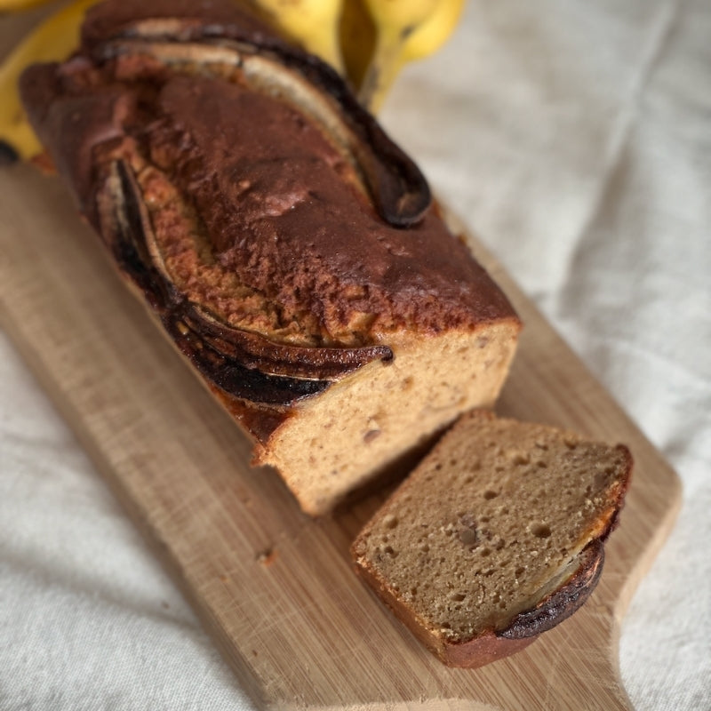 Loaf of banana bread with a slice cut, on a wooden board. Gluten Free Vegan Banana Bread with Sprouted Walnuts - 550g