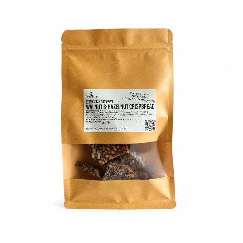 A stand-up kraft paper pouch of Gluten Free Walnut & Hazelnut Crispbread - 180g, featuring a clear window at the bottom that displays the Gluten Free Walnut & Hazelnut Crispbread - 180g pieces inside. The packaging is a warm golden-brown color with a white label in the center.