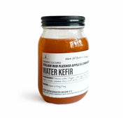 A glass jar of Italian Red Fleshed Apple & Cinnamon Water Kefir - 400ml (Foodcraft Online Store) with a black metal lid and a white label, containing an amber-colored probiotic drink, set against a plain white background.