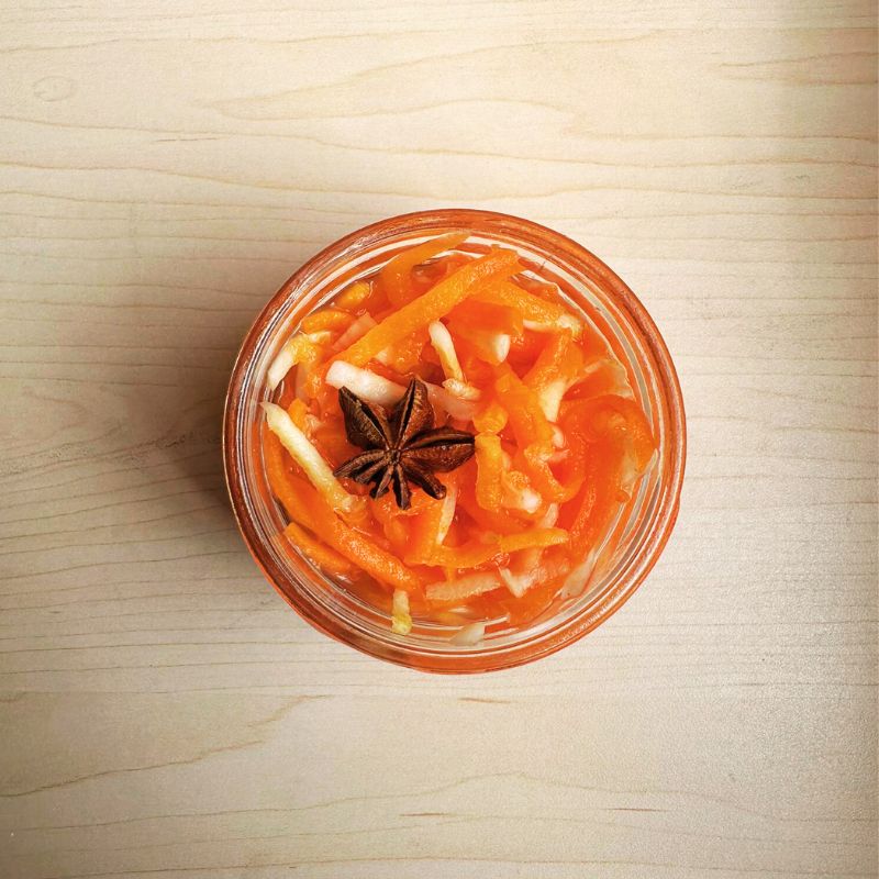Jar of Living Lacto-Fermented Carrots with Celeriac with a star anise on a wooden surface