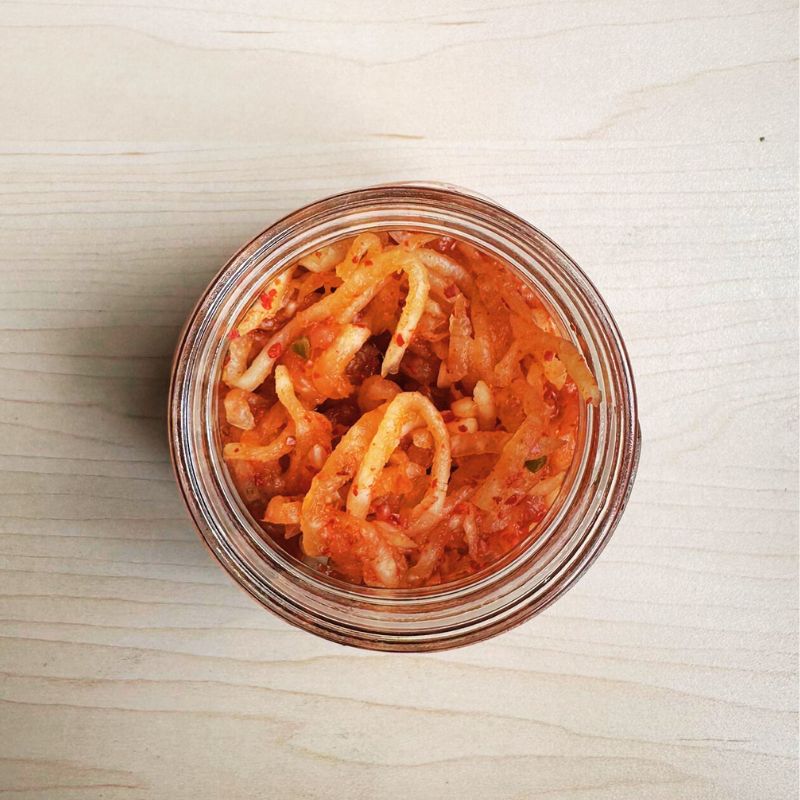 Glass jar filled with Living Lacto-Fermented Kimchee Daikon on a light wooden surface