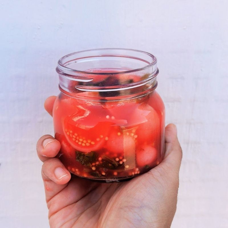 Hand holding a jar ofLiving Lacto-Fermented Radish with Mustard Seeds against a light background