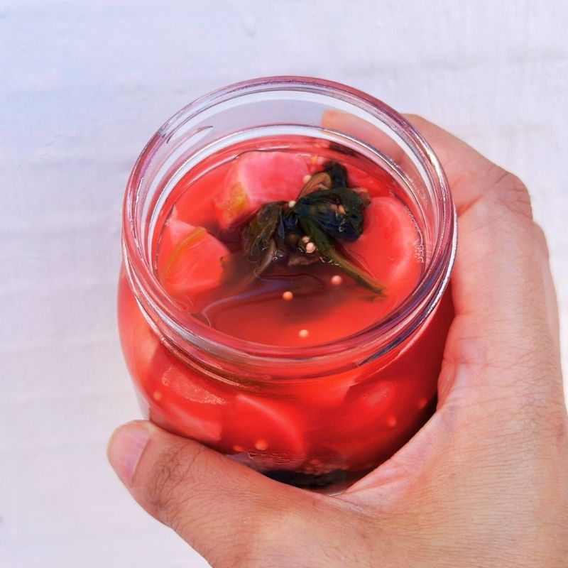 Hand holding a jar ofLiving Lacto-Fermented Radish with Mustard Seeds on a white background