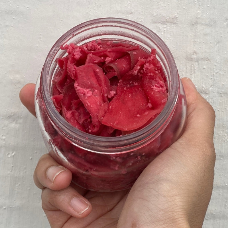 Hand holding a jar of Living Lacto-Fermented Watermelon Radish Koji Zuke on a light gray background
