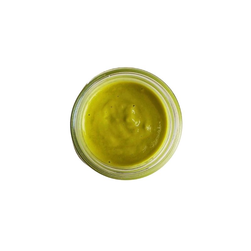 A top-down view of a small clear glass jar filled with thick Living Probiotic Creamy Jalapeno Sauce - 200g, centered on a plain white background.