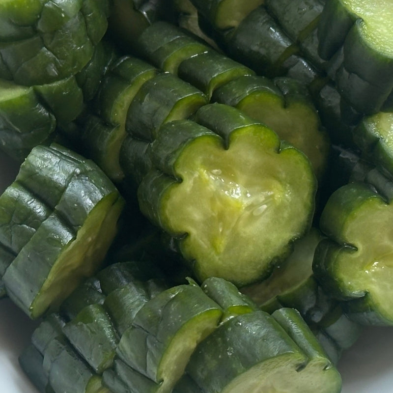 Close-up of sliced Living Probiotic Nukazuke Cucumber Pickles - 160g  with distinctive wavy edges, showing pale yellow-green interiors and a glossy surface.