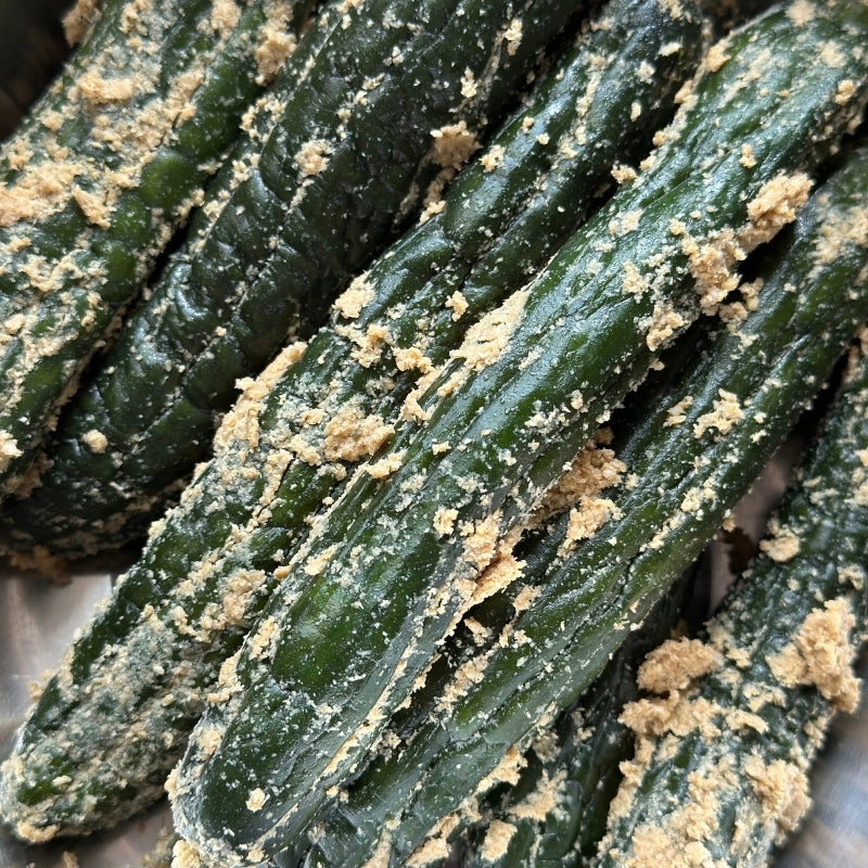 Close-up of several dark green cucumbers coated with nukazuke (japanese rice bran) filling the frame.