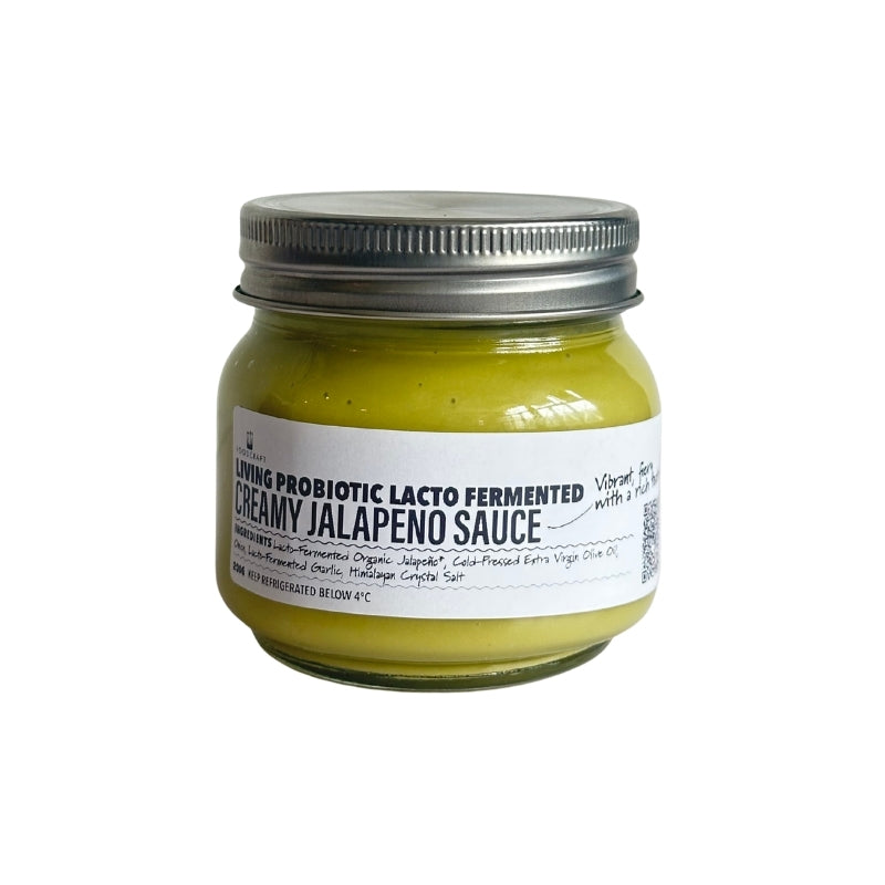 A small clear glass jar filled with Living Probiotic Creamy Jalapeno Sauce - 200g, sealed with a black metal screw lid, centered on a plain white background.