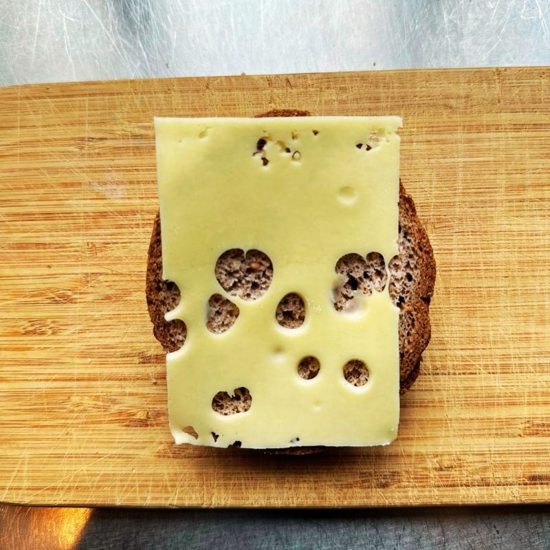 Swiss cheese with holes on a slice of Low Carb Keto Bun on a wooden cutting board