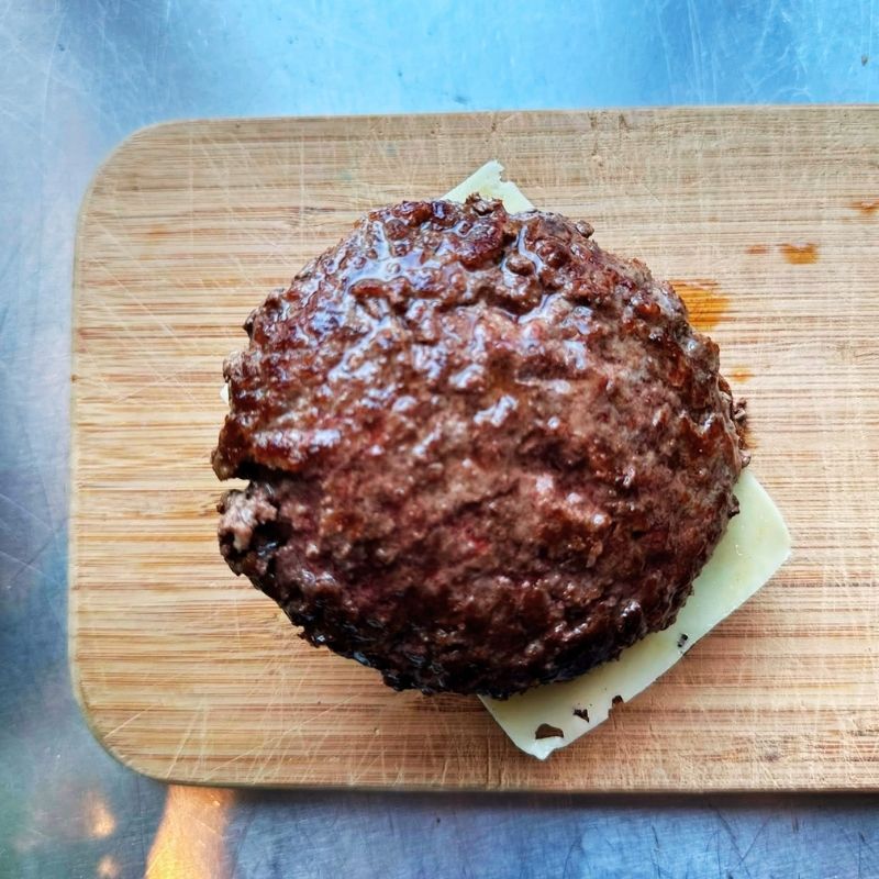 Hamburger patty on a piece of cheese on a wooden cutting board with a blue background