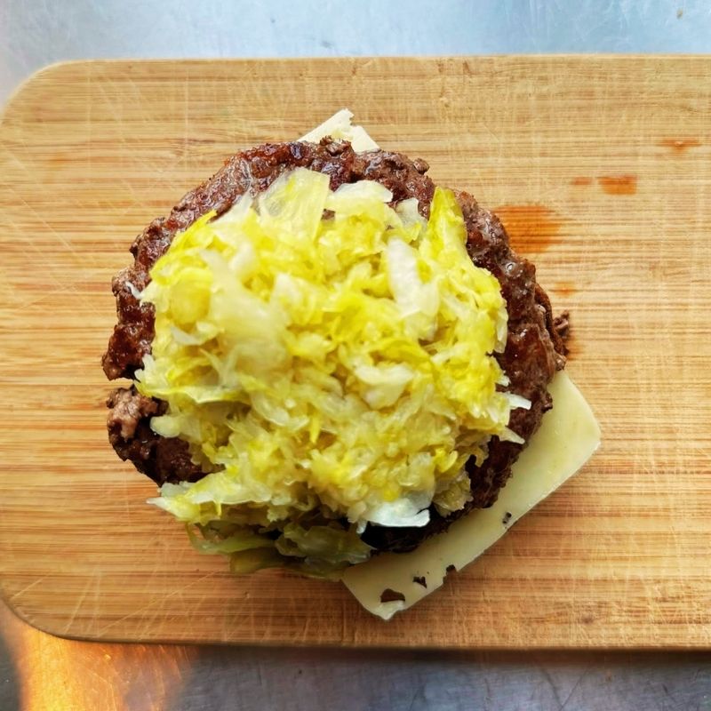 Hamburger patty with sauerkraut and cheese on a wooden cutting board