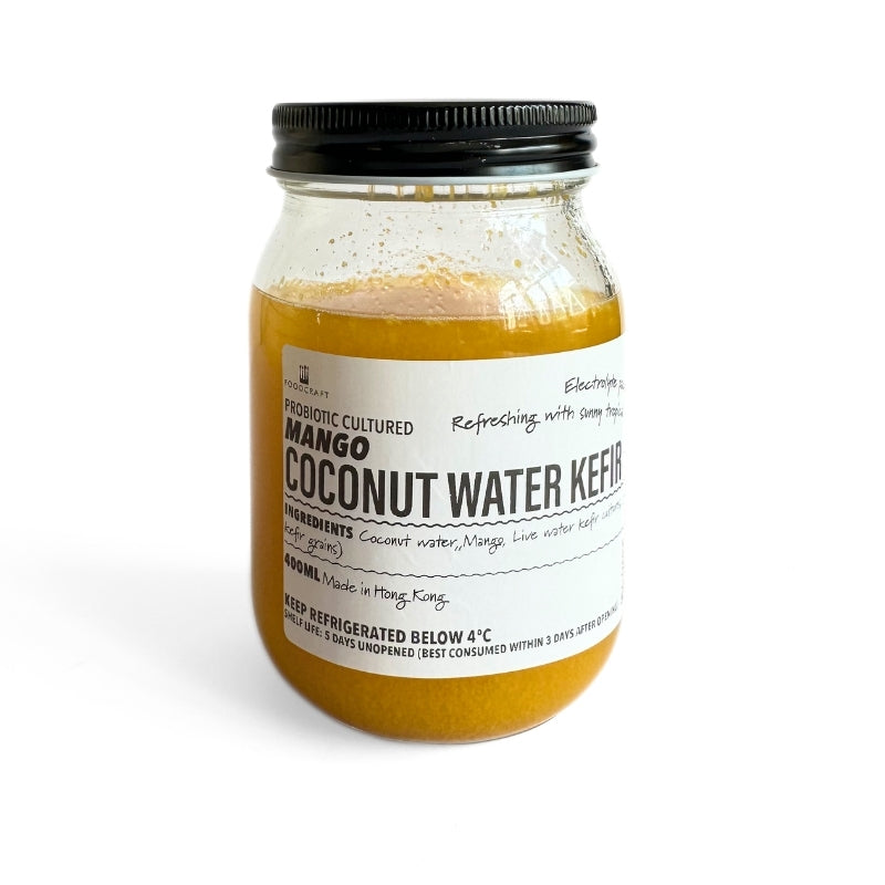 A glass jar of Probiotic Cultured Mango Coconut Water Kefir  featuring a white label and a black metal screw cap, set against a plain white background.