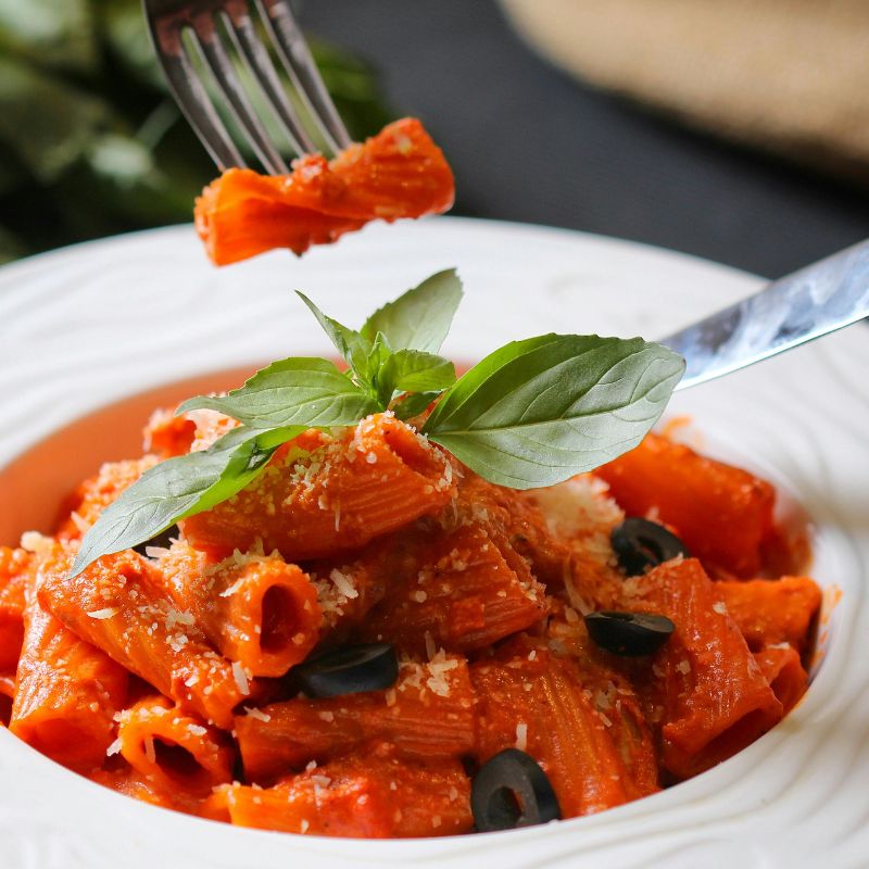 Pasta dish with Mr Organic Italian Organic Cherry Tomato Pasta Sauce (No Added Sugar) , olives, and basil leaves in a white bowl.