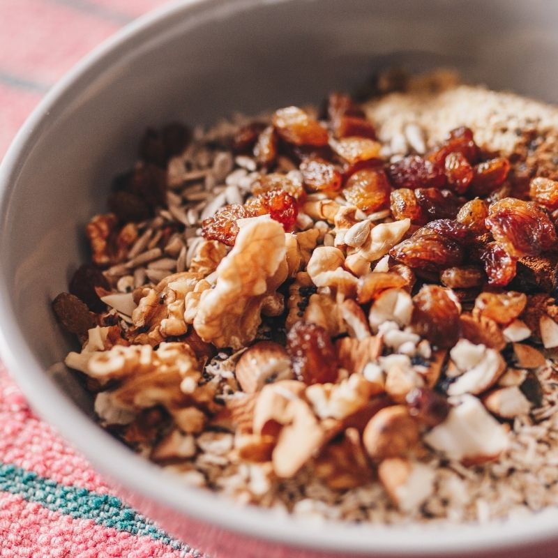 Close-up of a bowl filled with a mixture of nuts and dried fruits and Organic Wholegrain Rolled Oats on a textured surface.
