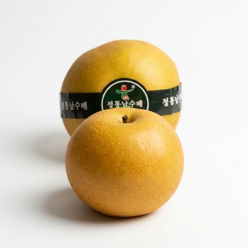 Two golden-yellow Nashi Pears from Korea on a clean white background, with one pear in the foreground and another behind it wrapped in a black label with Korean text and a small green logo.