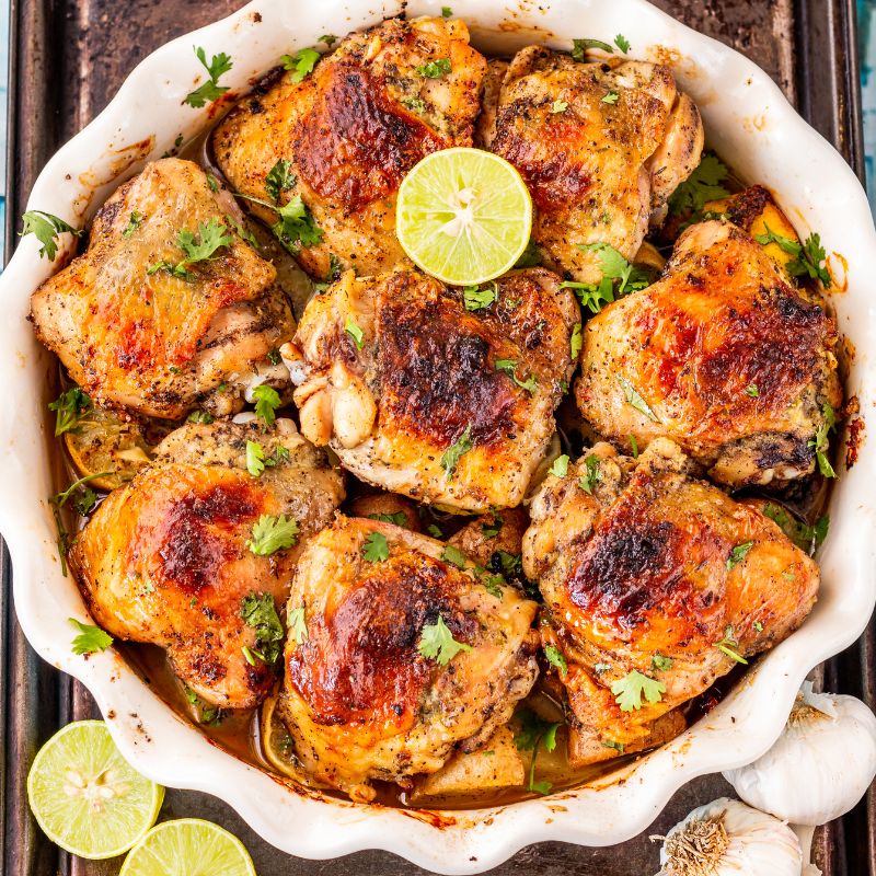 Baked Pasture Raised Yellow Chicken Thigh Boneless with lime wedges and herbs in a white dish.