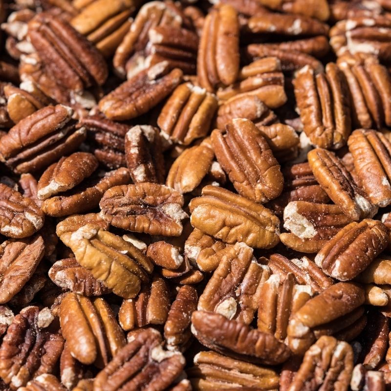 A close-up pile of whole  raw sprouted pecans with rich brown and tan tones filling the frame.