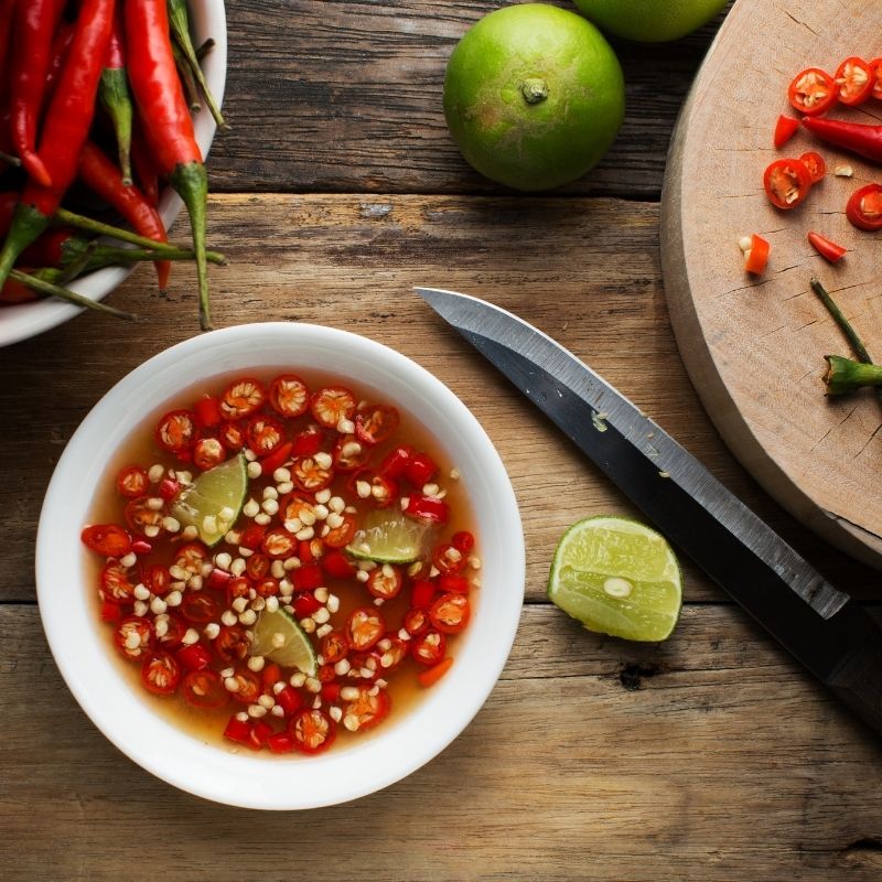 fish sauce with red peppers and limes on a wooden table