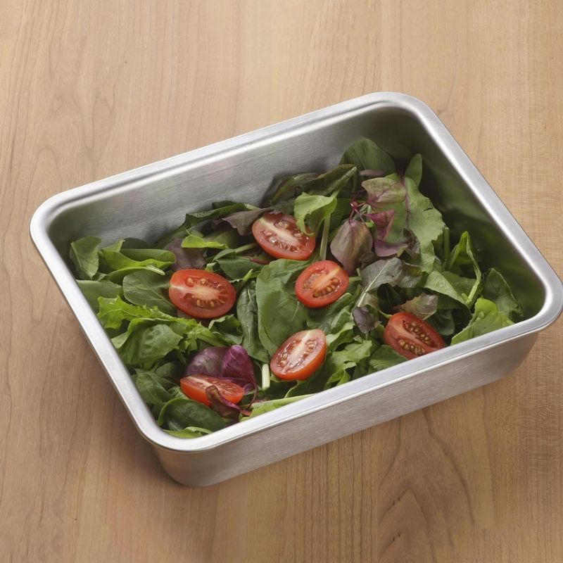 Stainless Steel Storage Prep Tray with Lid (Wide Deep Size) filled with a green salad containing sliced red tomatoes, placed on a light wood tabletop.
