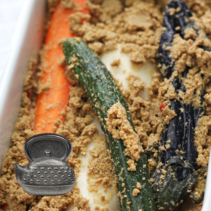 Close-up of a nukadoko with carrots, cucumber, eggplant, daikon radish and Takaki Metal Cast Iron Egg for Nukadoko in a white container.