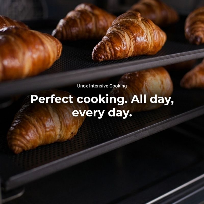 Croissants baking on XEFR-04EU-ETDP UNOX-BAKERLUX SHOP.Pro™ TOUCH Oven with pump-4 trays dark oven racks, with overlaid text reading 'Unox Intensive Cooking' and 'Perfect cooking. All day, every day.