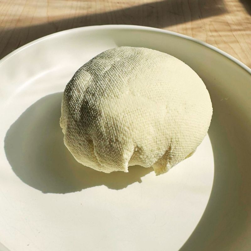 Ball of Foodcraft Vegan Almond Ricotta Cheese on a white plate with a wooden background