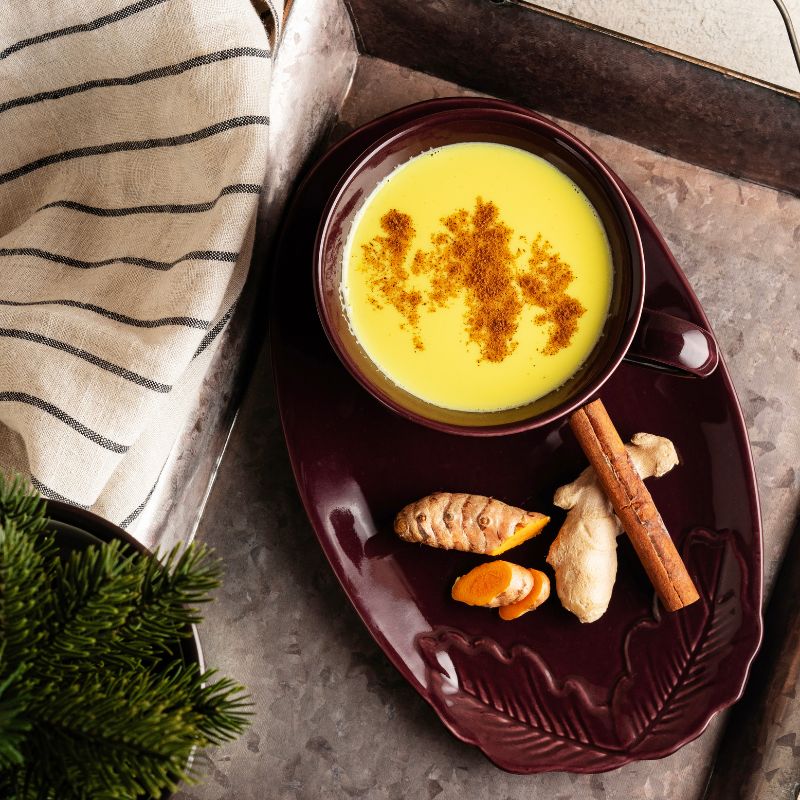 Mug of turmeric golden milk with spices on a dark plate, placed on a textured surface with a striped cloth.