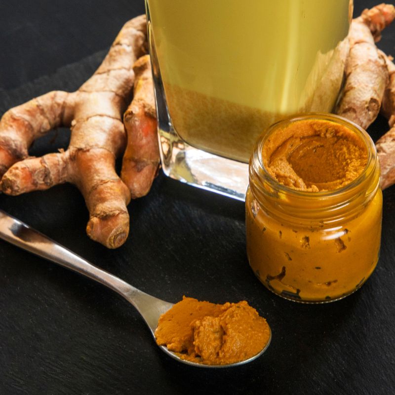 Turmeric root, jar, and spoon with turmeric paste on a dark surface
